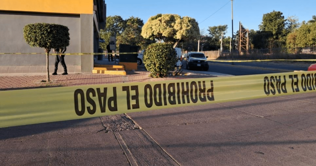 Cinta de restricción 'PROHIBIDO EL PASO' en Culiacán, con vehículos y personas al fondo.