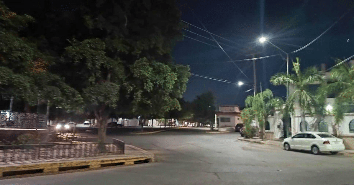 Calle nocturna en Culiacán con árboles, luces de calle y un automóvil blanco estacionado.