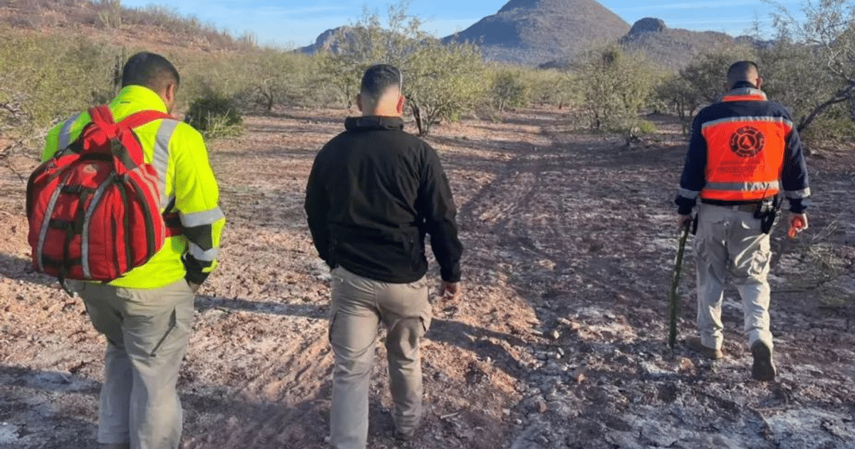 Tres personas en ropa de seguridad caminan en un paisaje desértico, posiblemente en una misión de búsqueda.