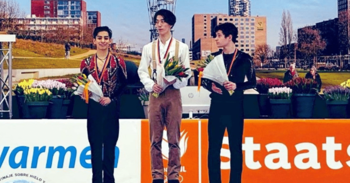 Tres patinadores sobre hielo en el podio del Challenge Cup 2025, sosteniendo flores y medallas, con un fondo de edificios y flores.