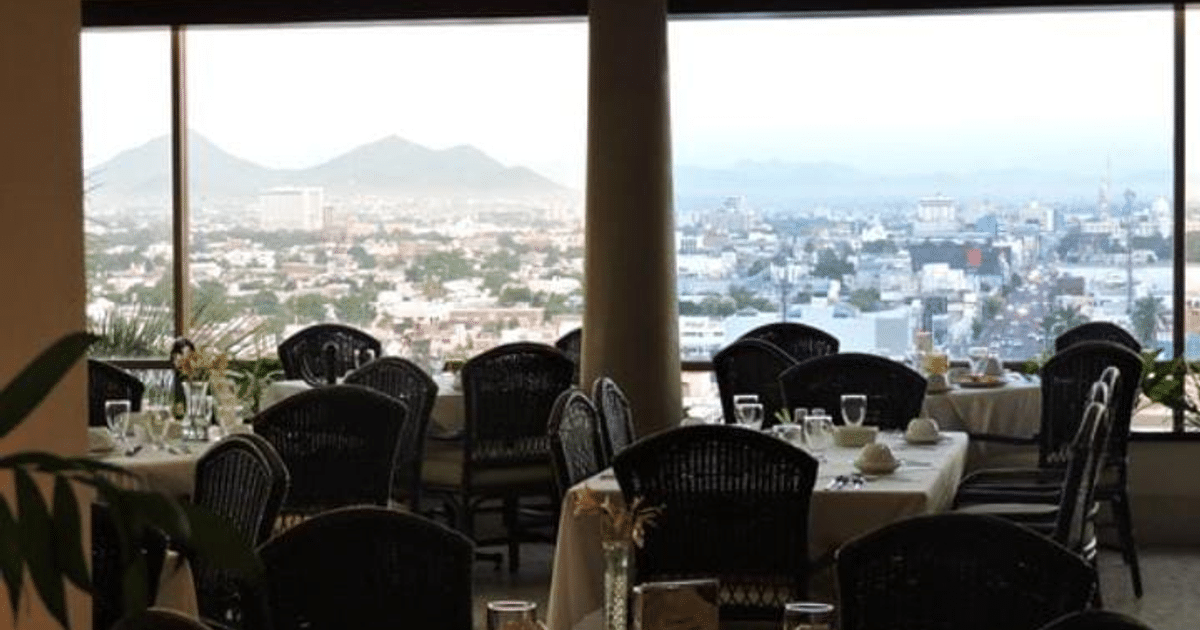 Interior del restaurante El Mirador con mesas preparadas y vista panorámica de la ciudad y montañas.