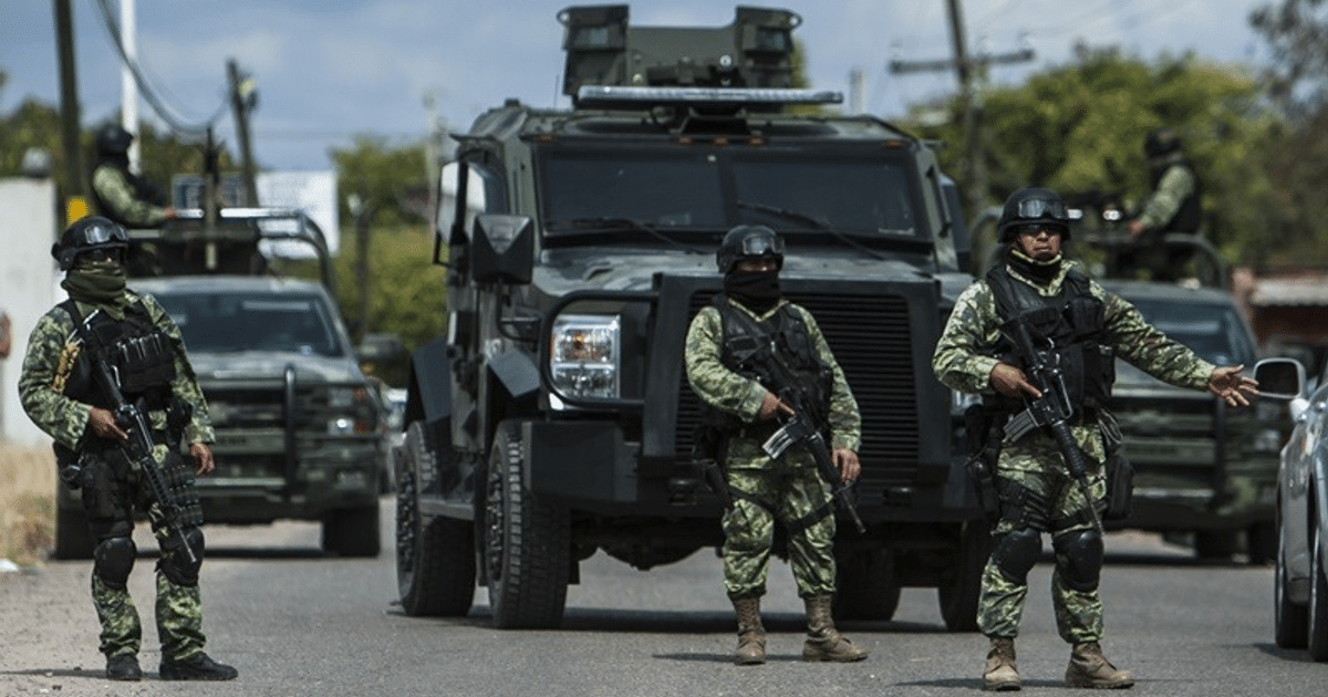 Soldados armados en operativo de seguridad en Teacapán, Sinaloa, con vehículos blindados en el fondo.