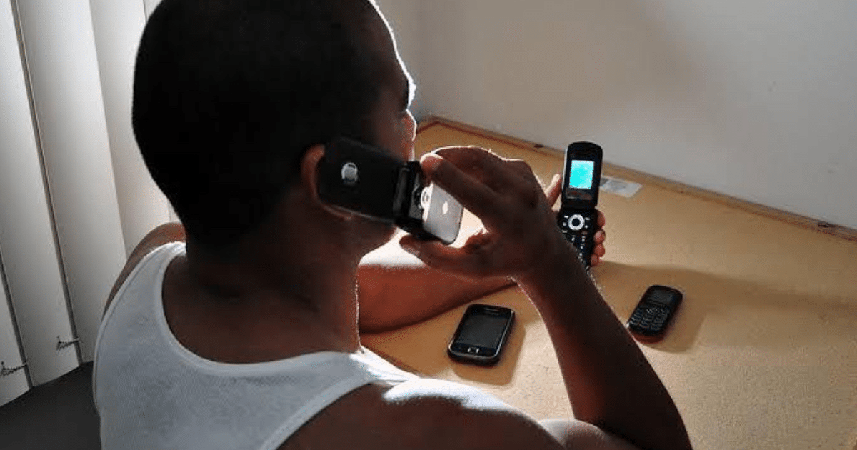 Persona hablando por un teléfono móvil mientras sostiene otro en un entorno doméstico, con varios teléfonos sobre la mesa.