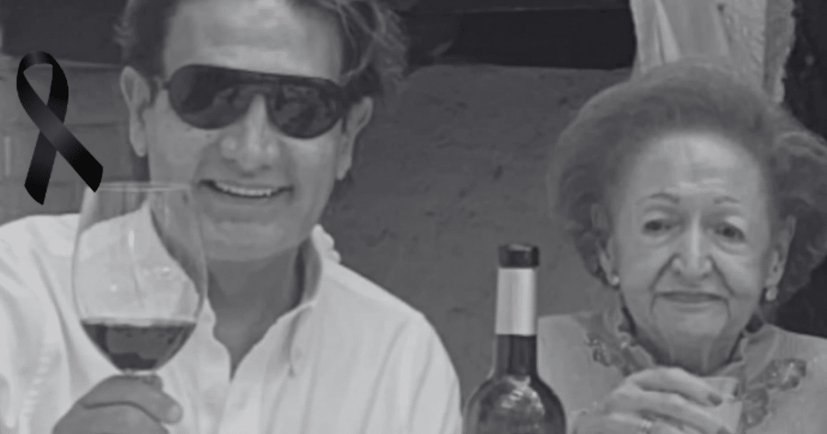 Dos personas en una mesa con una copa de vino y un lazo negro, simbolizando el luto por María Eugenia Kuri.