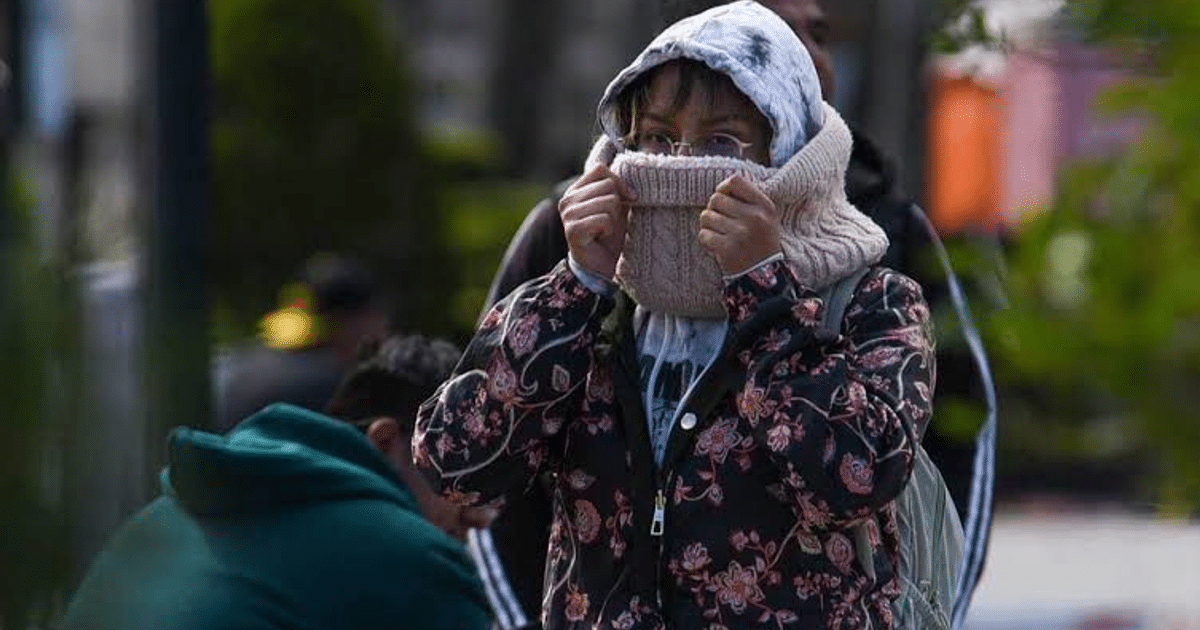 Persona con abrigo florido y bufanda en un día frío en la ciudad, con otras personas al fondo.