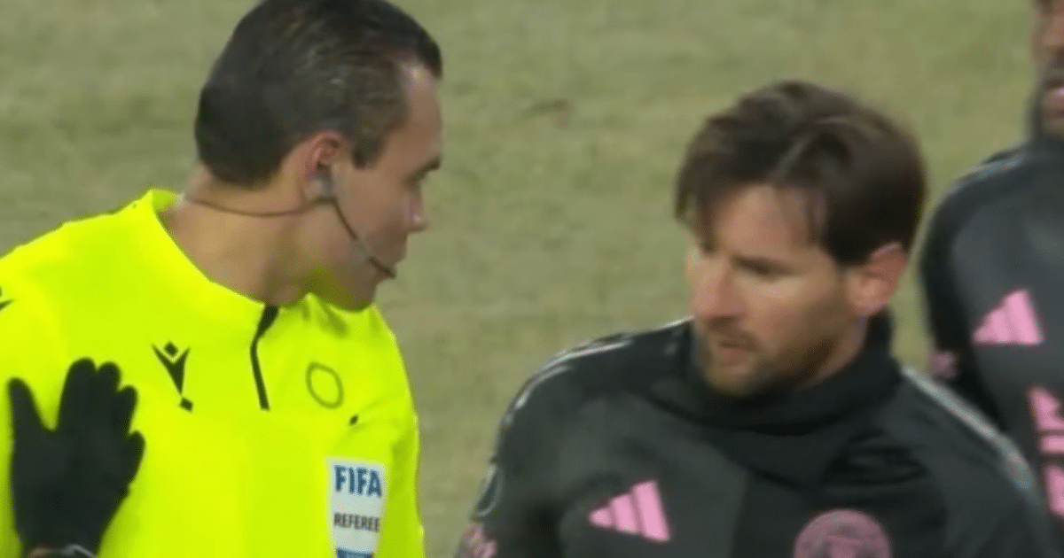 Árbitro de fútbol en uniforme amarillo hablando con jugador de camiseta oscura y detalles rosas