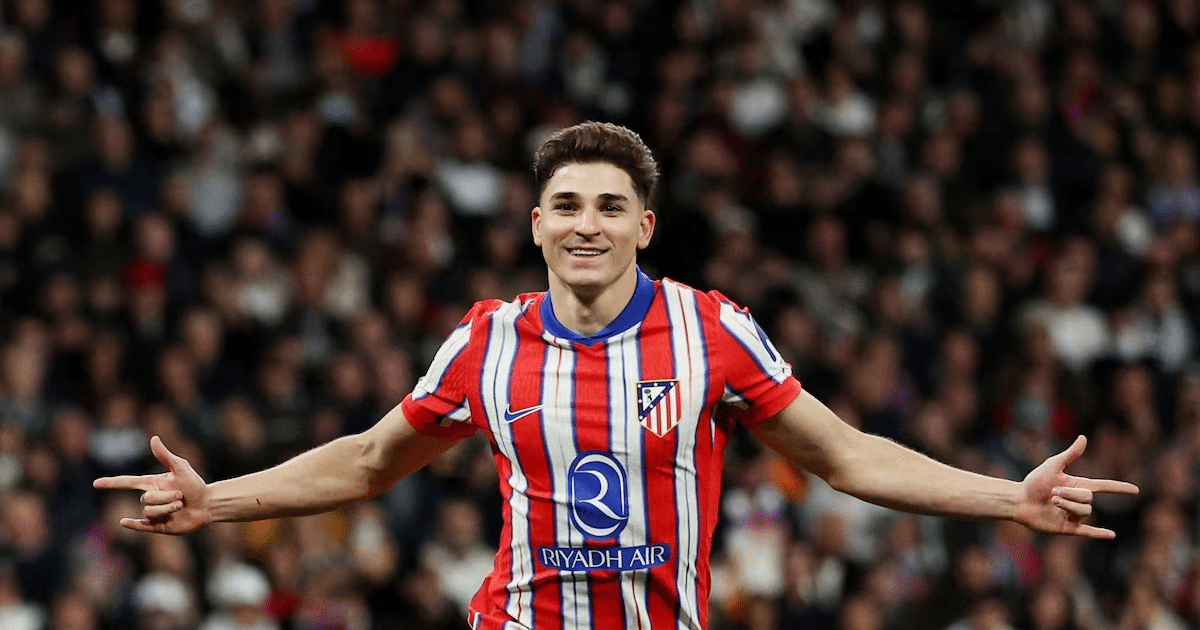 Julián Álvarez celebrando un gol con el Atlético de Madrid, sonriente y con los brazos extendidos, en un estadio lleno de aficionados.