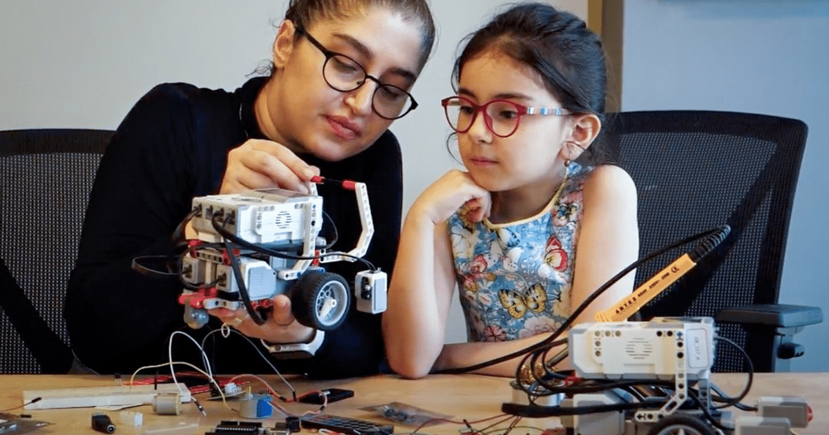 Mujer y niña colaborando en un proyecto de robótica, rodeadas de componentes electrónicos.