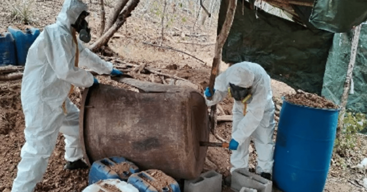 Dos personas con trajes de protección manejan un tambor en un operativo al aire libre contra narcolaboratorios.