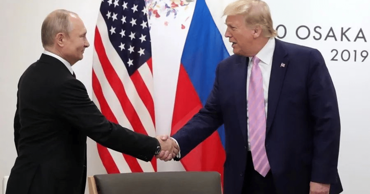 Dos personas dándose la mano con banderas de Estados Unidos y Rusia de fondo, representando un evento diplomático.