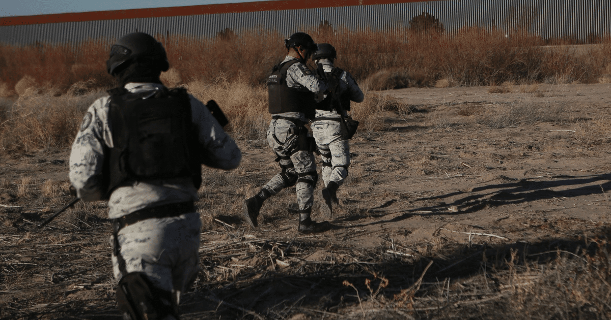 Efectivos de la Guardia Nacional en operativo de seguridad en Ciudad Juárez, con uniformes tácticos y un muro metálico al fondo.