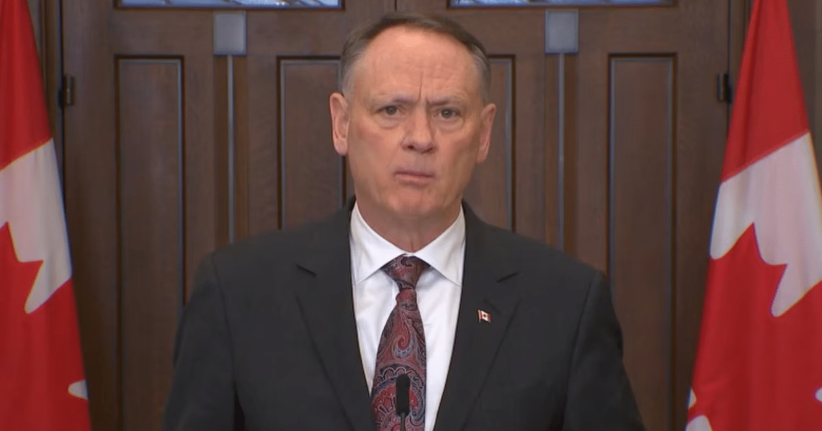 Persona hablando en conferencia de prensa en Ottawa con banderas canadienses de fondo
