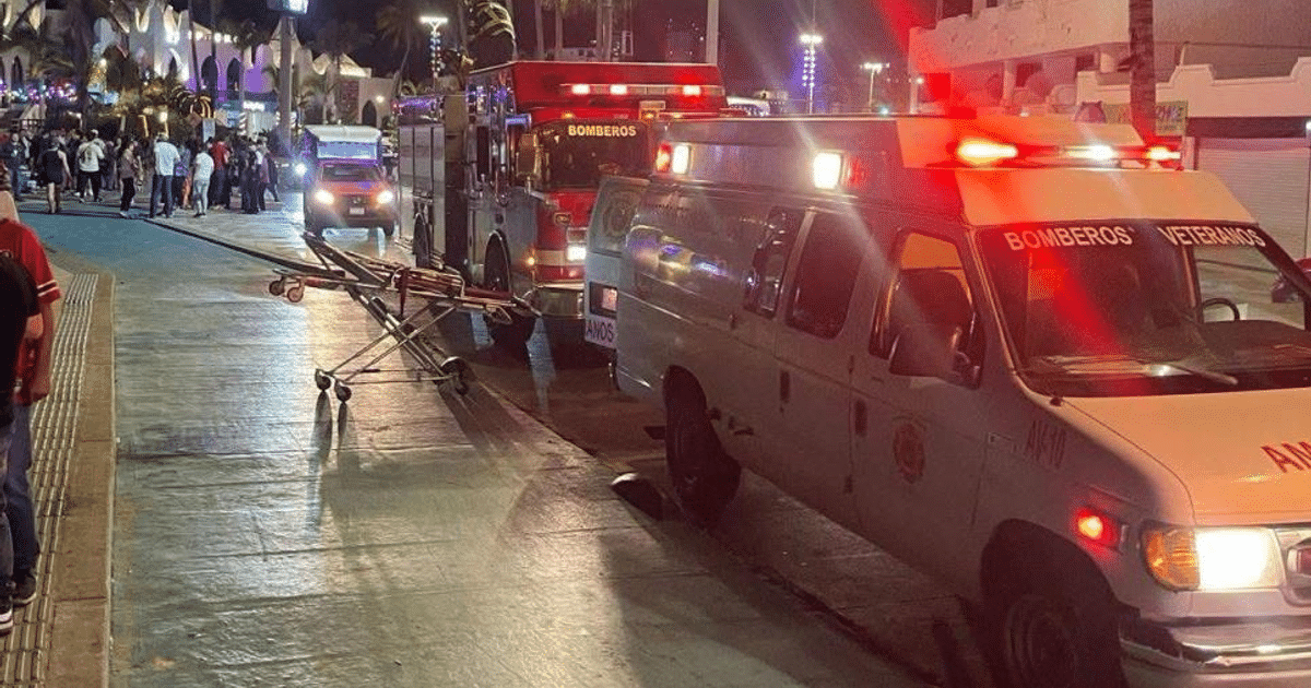 Escena nocturna de emergencia en el malecón con vehículos de bomberos y ambulancia.