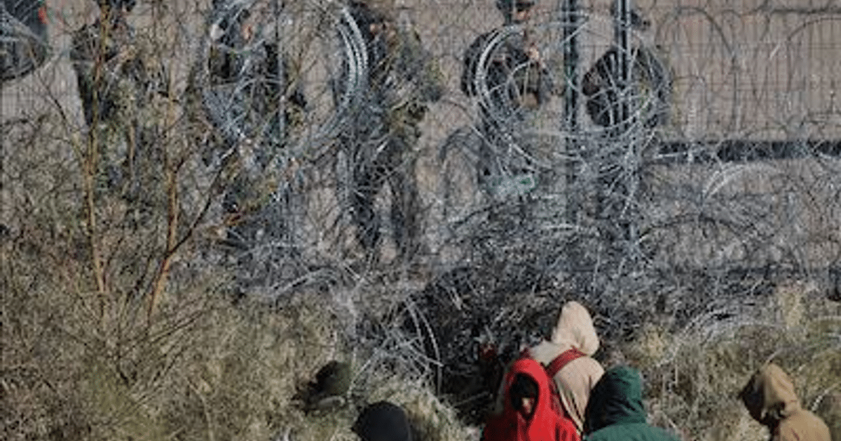 Personas con abrigos oscuros frente a una barrera de alambre de espino en un entorno militar.