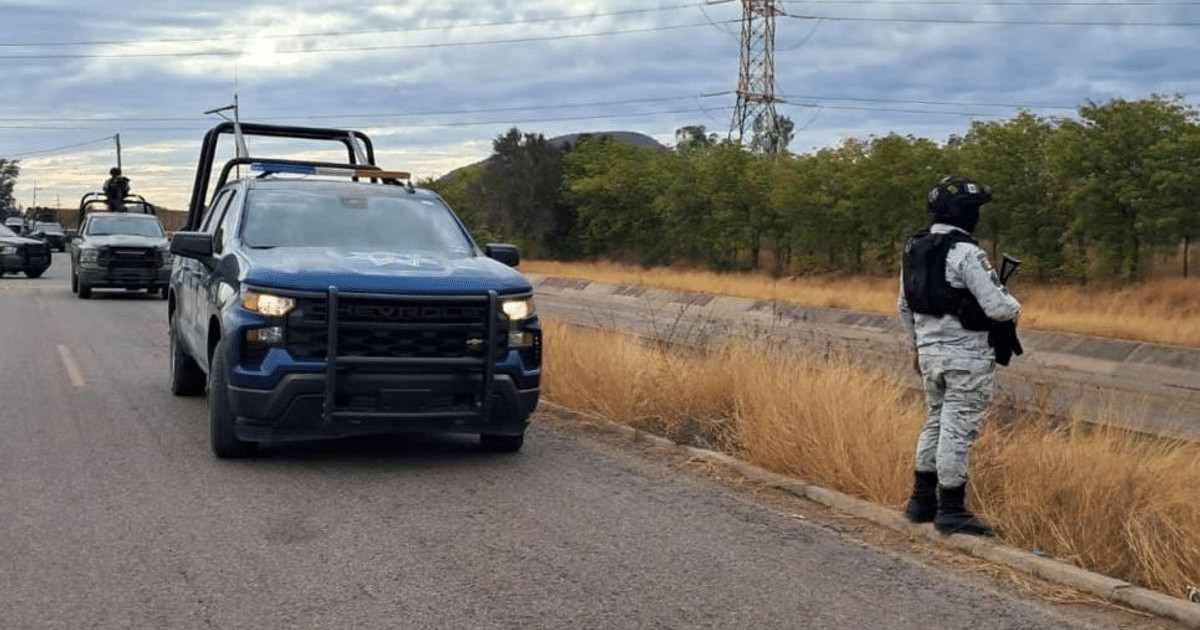 Camioneta de policía en operativo de seguridad en Culiacán, con hombre armado al lado de la carretera.