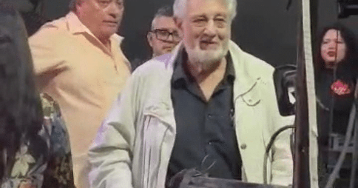 Plácido Domingo sonríe en un evento en Mazatlán, rodeado de personas en un ambiente festivo.