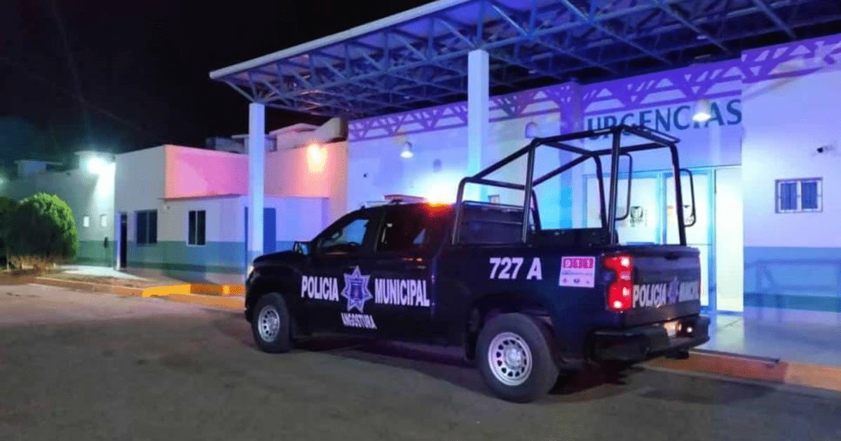 Vehículo de la Policía Municipal frente a un centro de urgencias nocturno, iluminado por luces de colores.