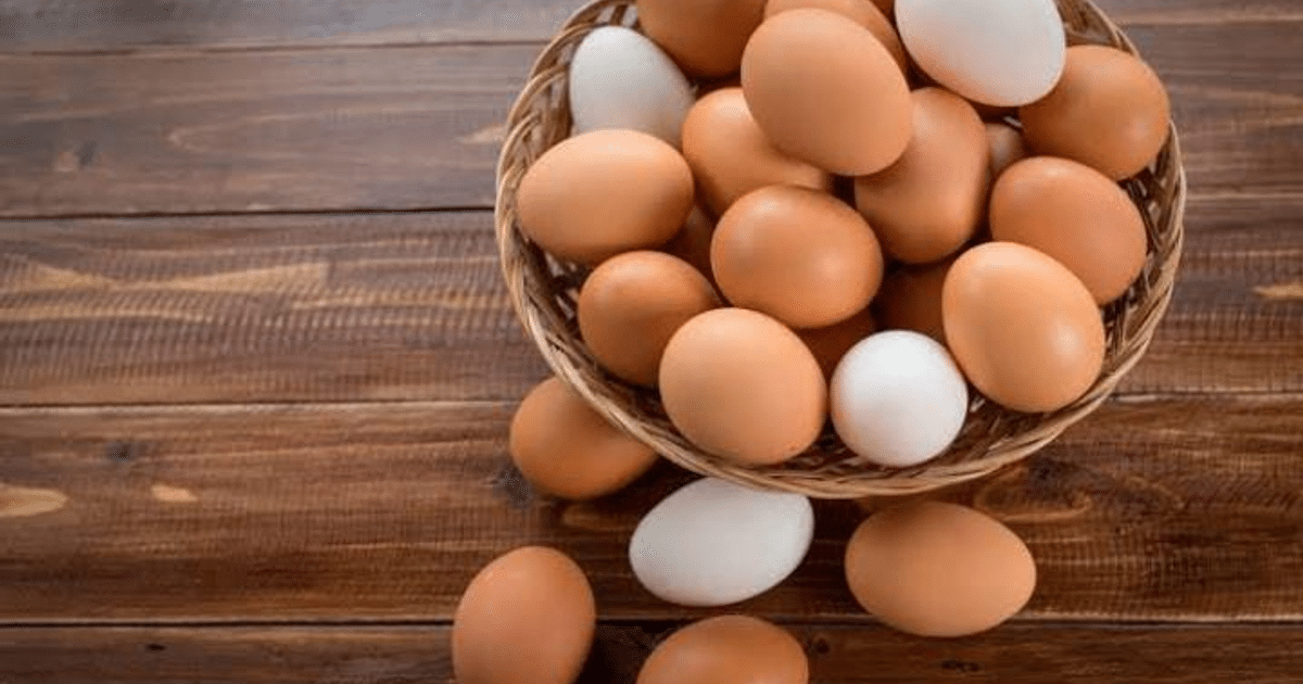 Cesta de huevos marrones y blancos sobre fondo de madera rústica