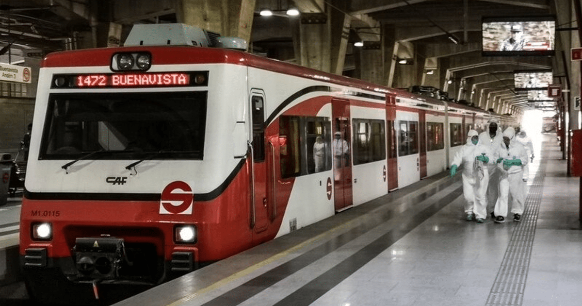 Tren de cercanías rojo y blanco en estación con personal de seguridad en trajes blancos.