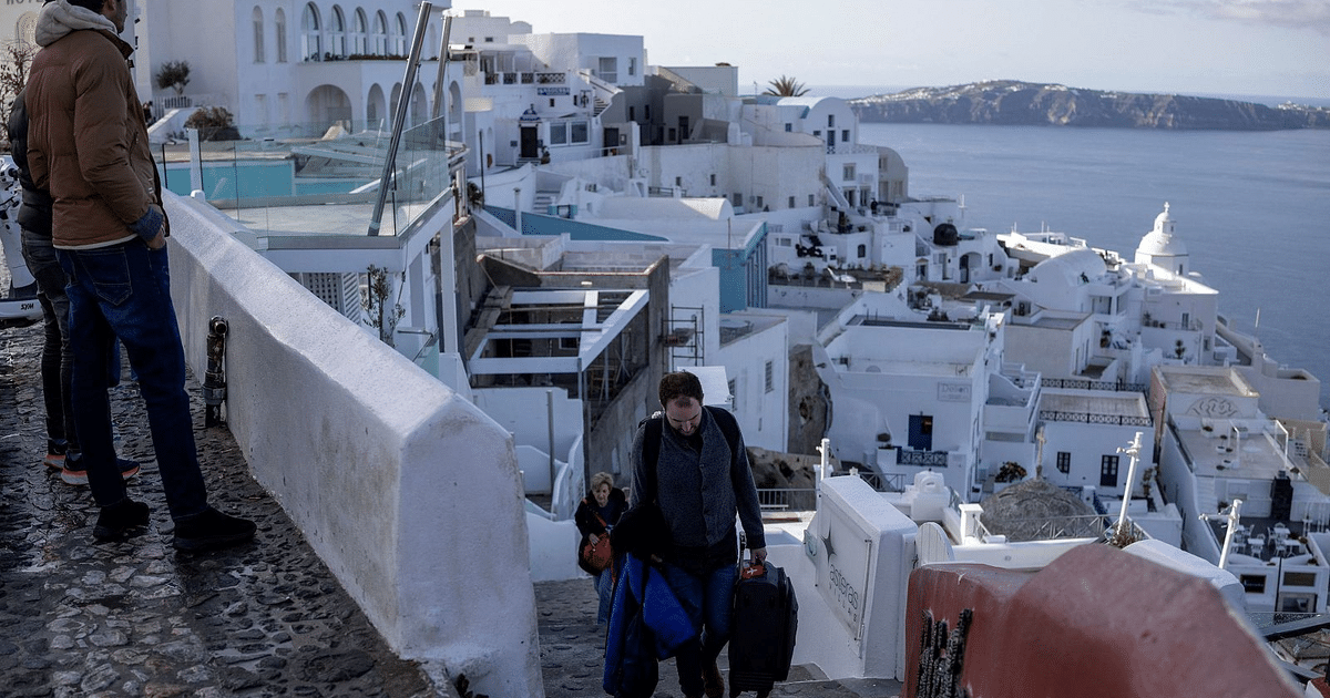 Vista de un paisaje urbano en Santorini con personas en un camino elevado y edificios blancos al fondo, durante un periodo de actividad sísmica.