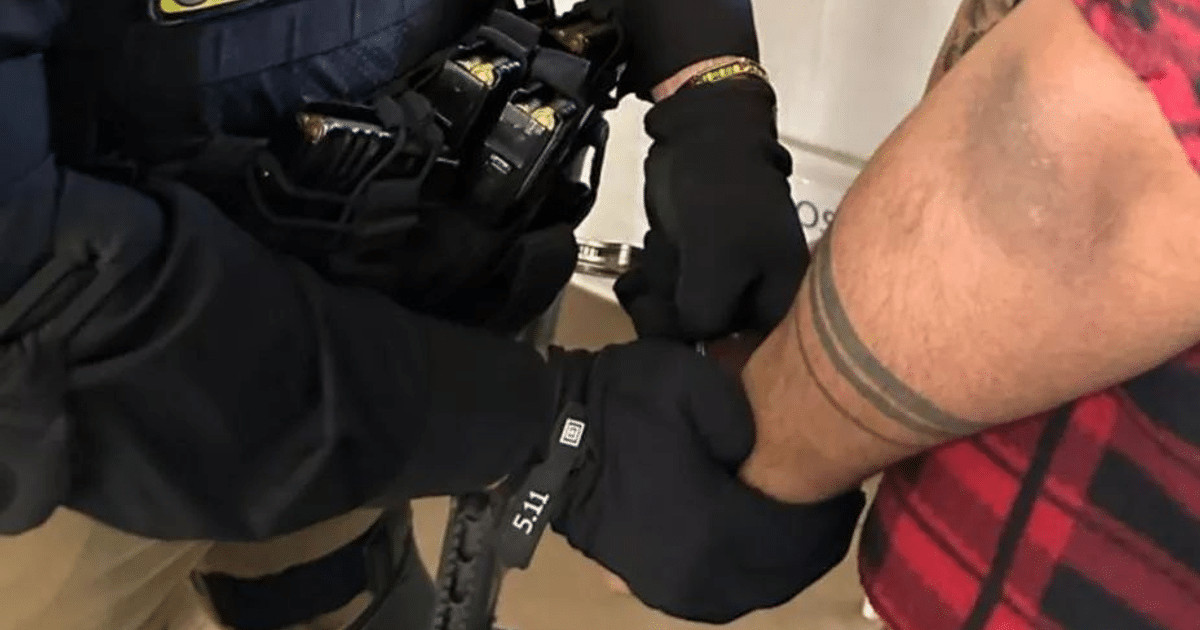 Agente de seguridad esposando a Ezequiel “N” con guantes, mostrando tatuajes en el brazo del detenido.