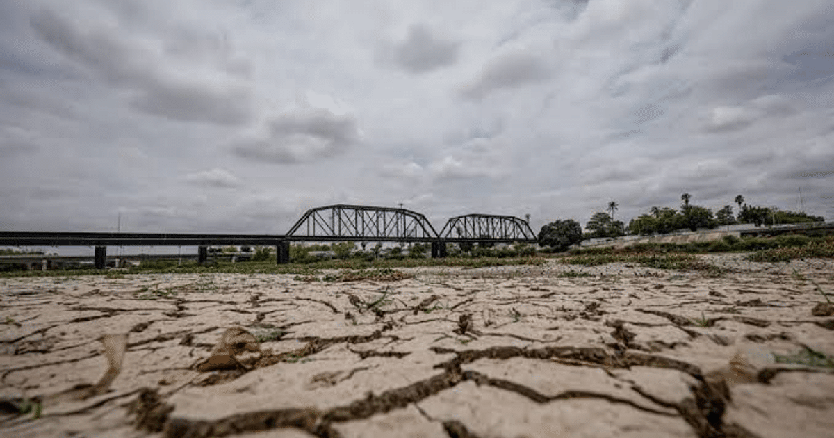 Paisaje seco en Sinaloa con puente de metal y cielo nublado, reflejando la sequía extrema en la región.