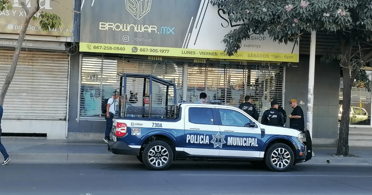 Camioneta de la Policía Municipal estacionada frente a un negocio en Culiacán, con personas alrededor y un árbol en primer plano.