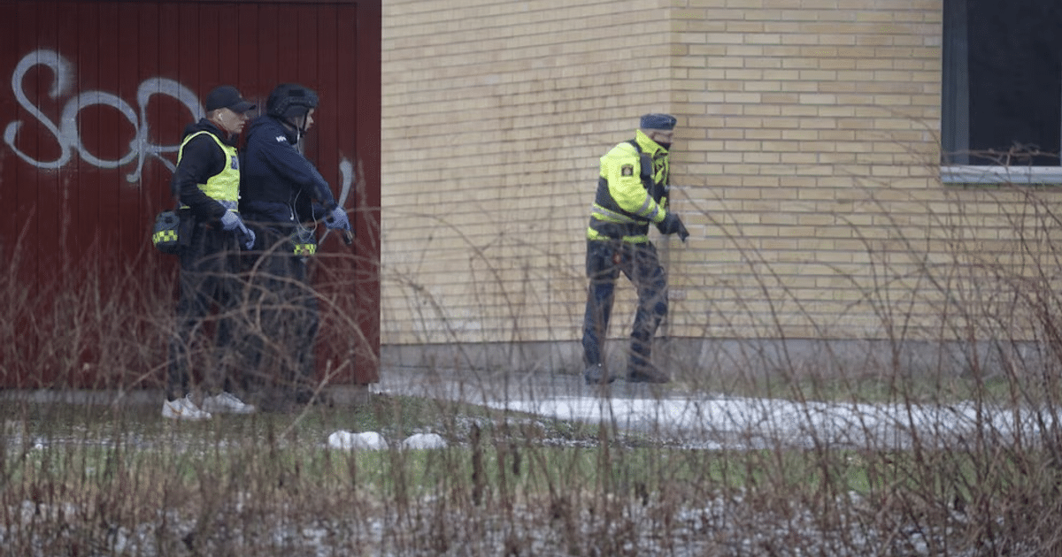 Agentes de policía en operativo cerca de edificio de ladrillos amarillos y puerta roja grafiteada tras tiroteo en Örebro.