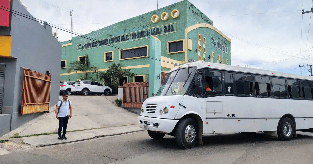 Autobús blanco en carretera urbana con edificio de transporte al fondo