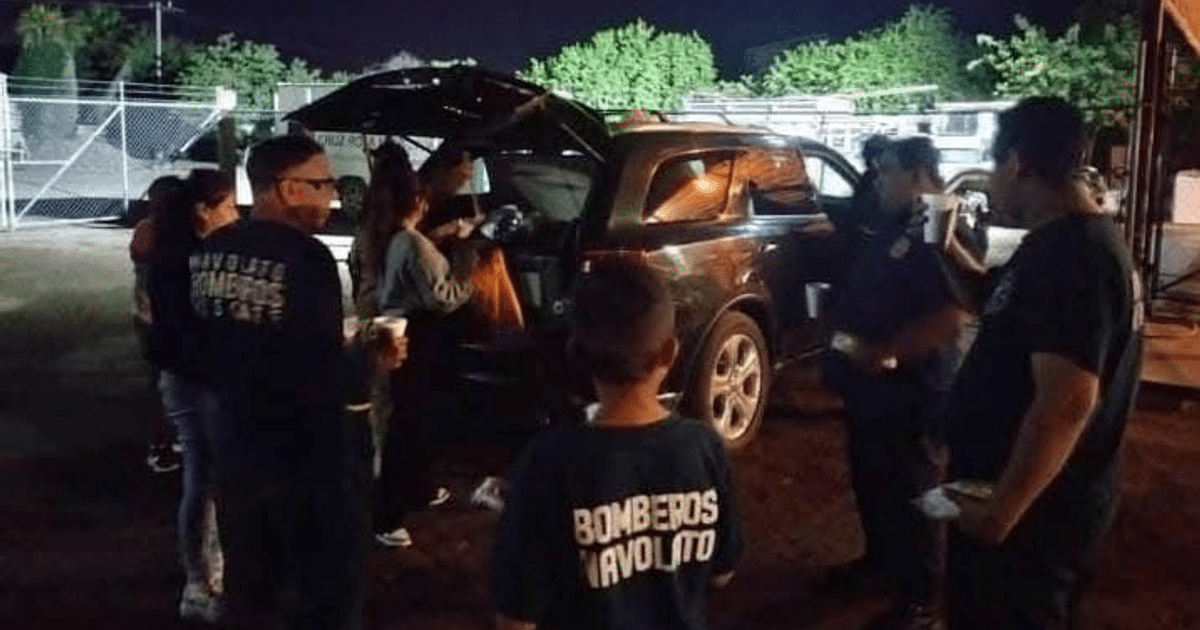 Bomberos y personas alrededor de un vehículo oscuro con maletero abierto en un accidente nocturno en Altata.