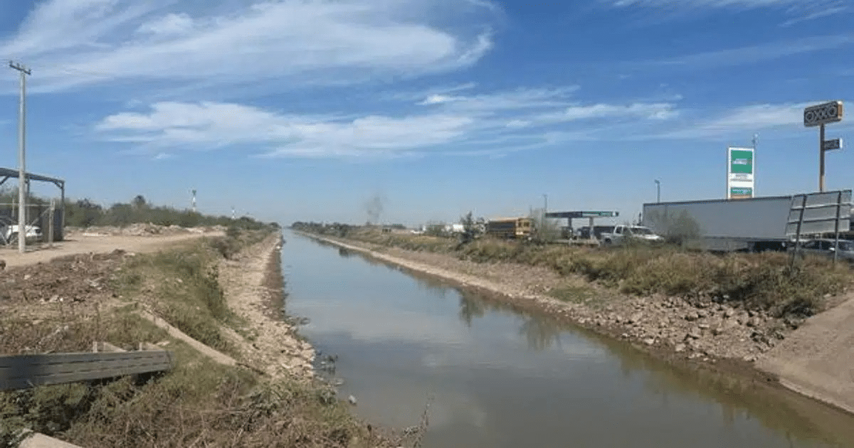 Canal de agua en Los Mochis con vegetación y estructuras urbanas al fondo, reflejando la situación de bajos niveles de agua.