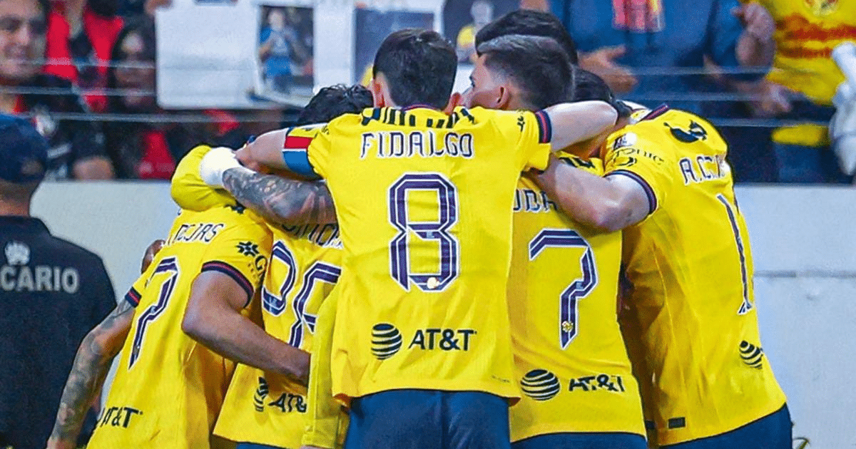 Jugadores del América celebrando el tercer gol en el estadio, con Fidalgo en el centro del abrazo.