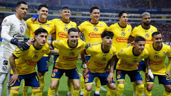 Equipo de fútbol con camisetas amarillas y pantalones azules posando en un campo de fútbol, con un estadio lleno de público al fondo.