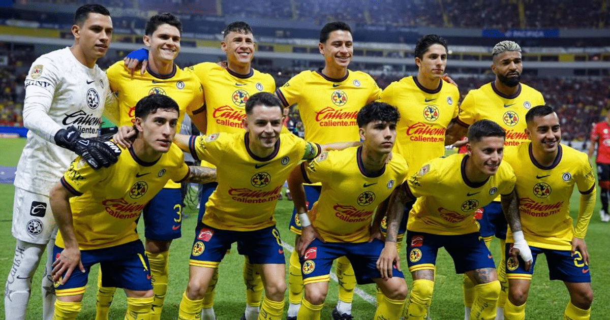 Equipo de fútbol con camisetas amarillas y pantalones azules posando en un campo de fútbol, con un estadio lleno de público al fondo.