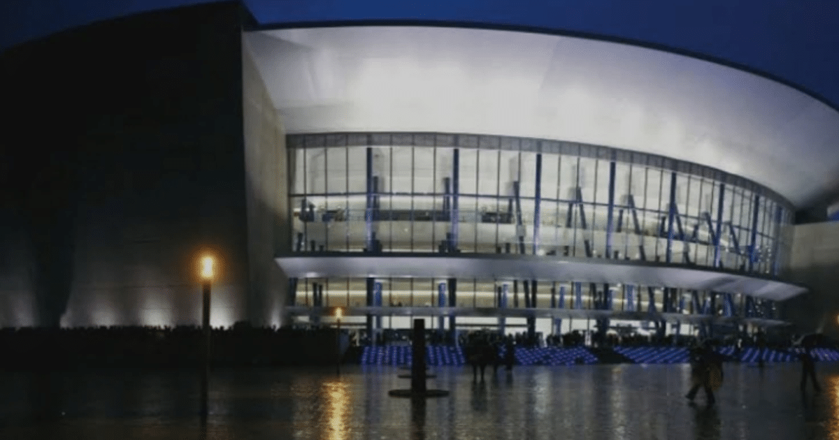 Edificio moderno iluminado al anochecer con personas en la entrada, posiblemente el Auditorio Telmex durante un evento cultural.