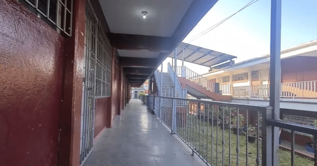 Pasillo de la Escuela Secundaria Técnica #85 con paredes rojas y suelo de cemento, iluminado por la luz del sol.