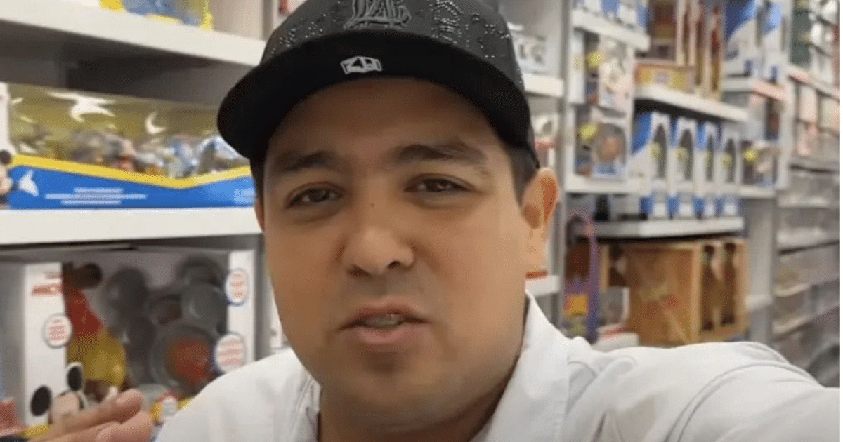 Hombre en tienda de juguetes hablando a la cámara con estanterías de productos al fondo.