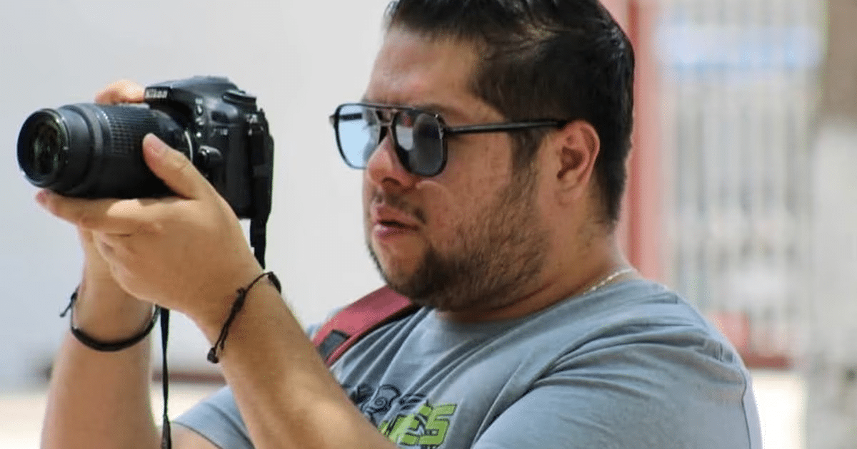 Persona con gafas de sol sosteniendo una cámara fotográfica al aire libre.