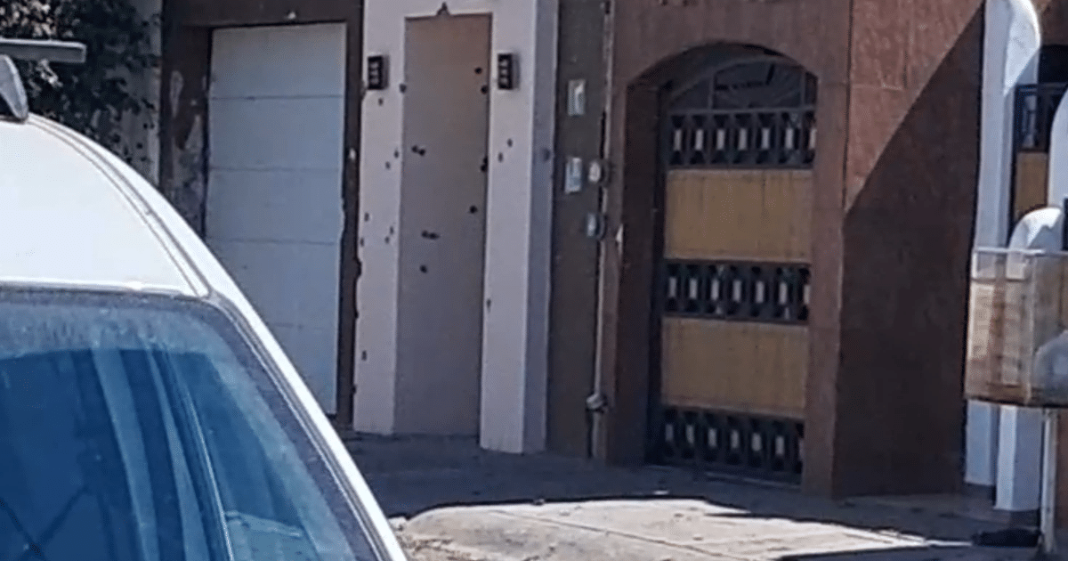 Imagen de una escena urbana en Culiacán con un automóvil, puerta con marcas de impactos y edificios residenciales.