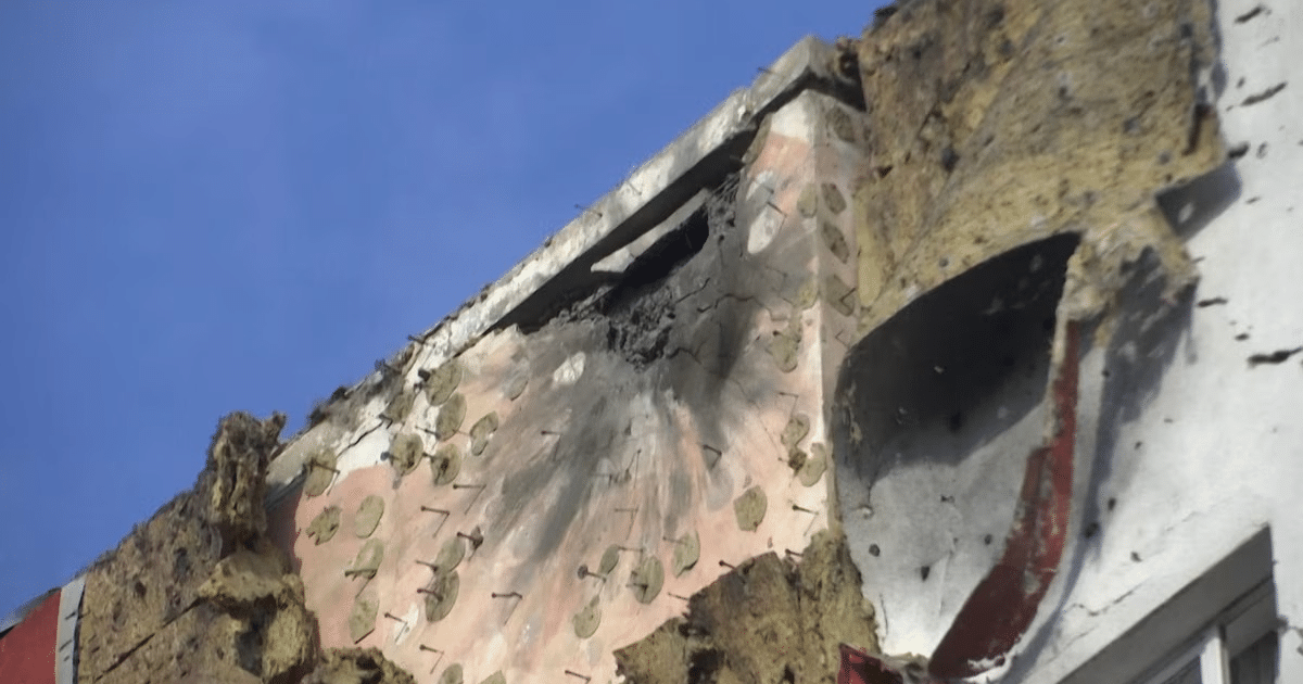 Sección dañada de un edificio tras ataque con drones, con agujero en la pared y materiales deteriorados, cielo visible al fondo.