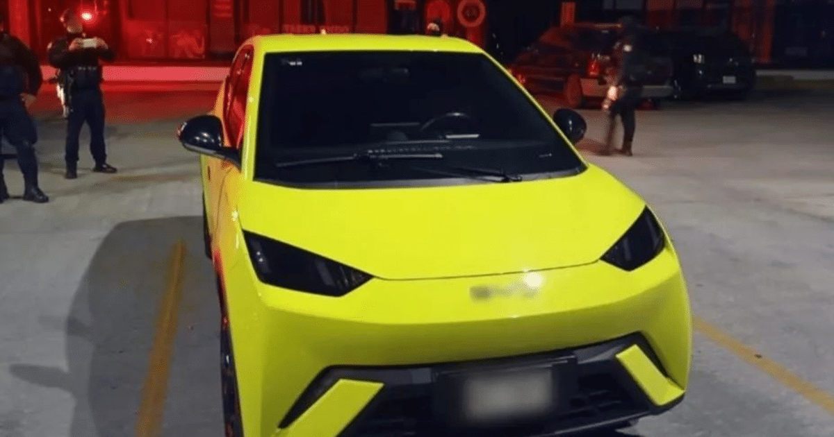 Automóvil amarillo brillante en operativo policial con luces rojas y policías al fondo.