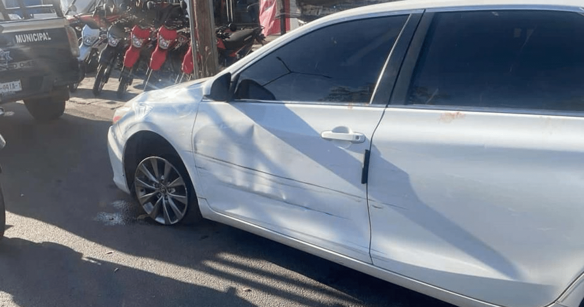 Automóvil blanco dañado con llanta desinflada y patrulla policial en el fondo en Culiacán.