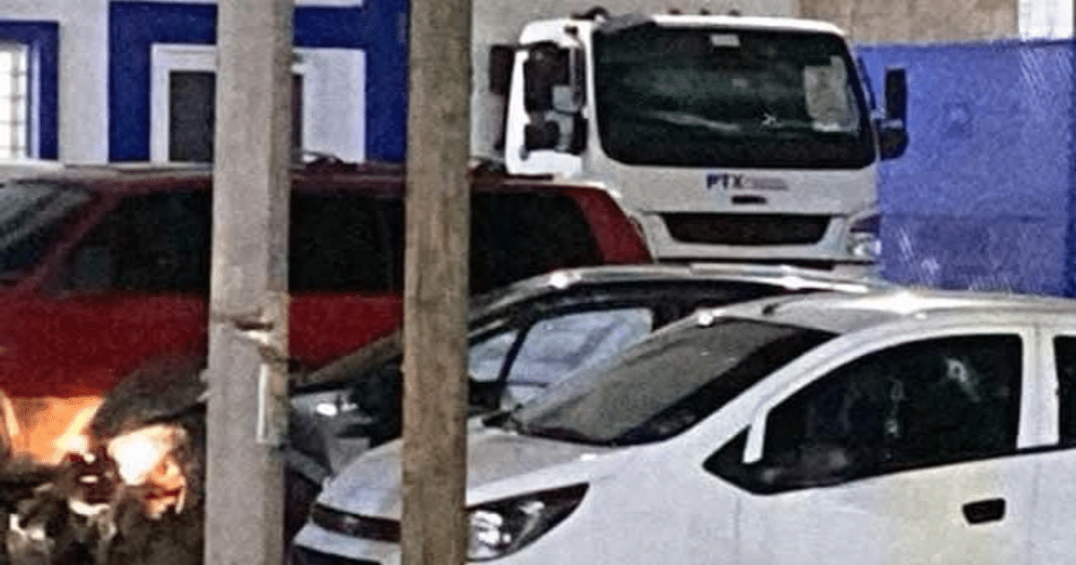 Vehículos estacionados en Culiacán tras incidente violento, con camión blanco y autos de colores, poste de luz y edificio azul y blanco de fondo.