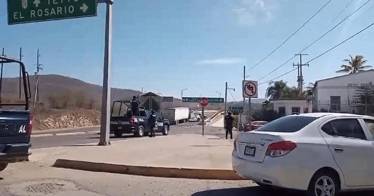 Carretera con control de tráfico y vehículos policiales en dirección a El Rosario, con montañas al fondo.