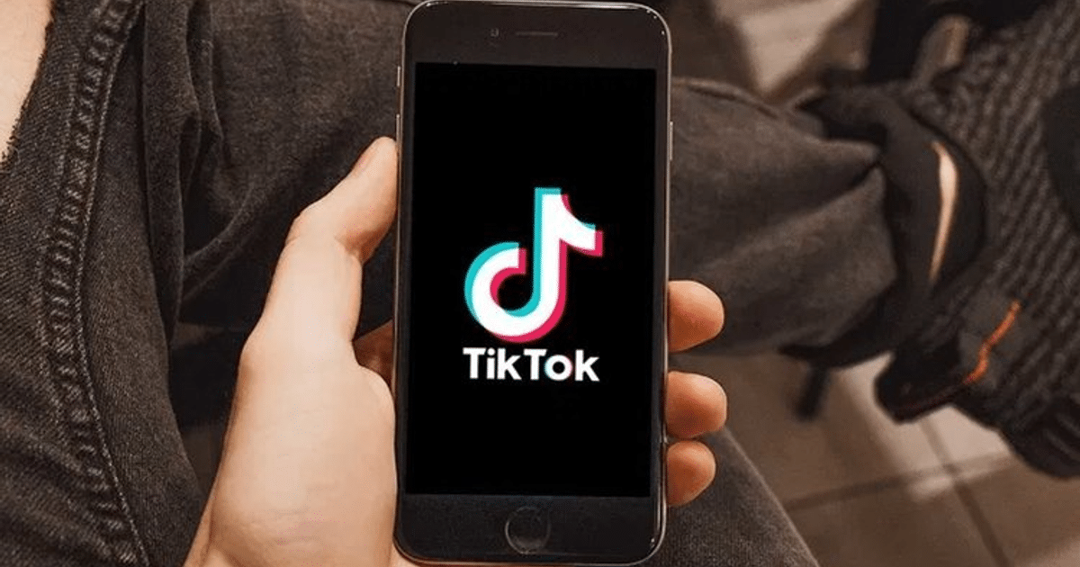 Teléfono móvil con logo de TikTok en pantalla, sostenido en una mano, fondo oscuro