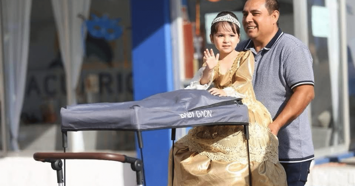Padre sonriente y niña en vestido dorado en cochecito durante desfile en Mazatlán
