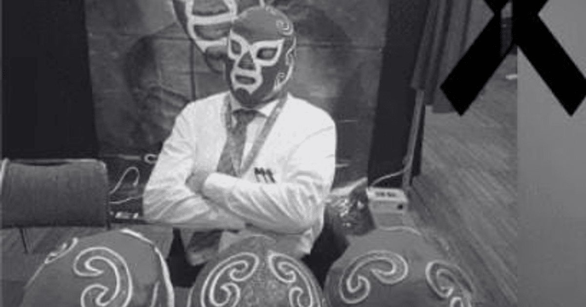 Persona con máscara de luchador y corbata, sentada frente a tres máscaras rojas, con un lazo negro a la derecha, en homenaje a Ciclón Ramírez.