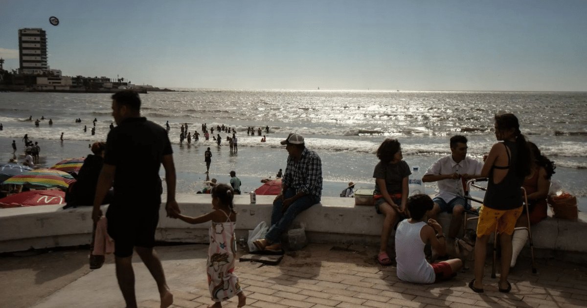 Personas disfrutando de un día soleado en la playa de Sinaloa, con sombrillas de colores y un mar tranquilo.