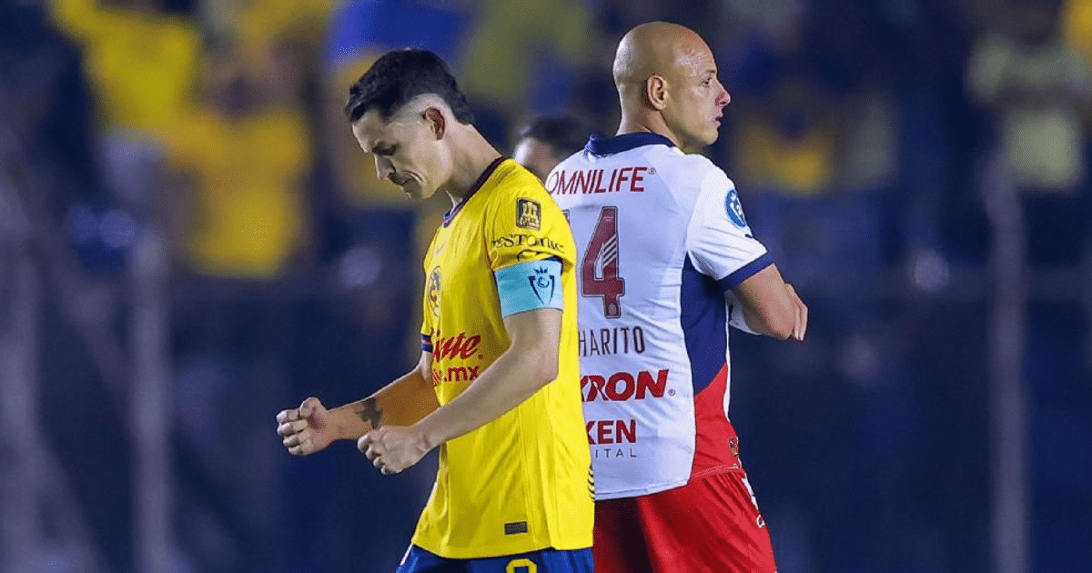 Dos jugadores de fútbol en un campo, uno con camiseta amarilla y brazalete de capitán, el otro con camiseta blanca, ambos en actitud pensativa.