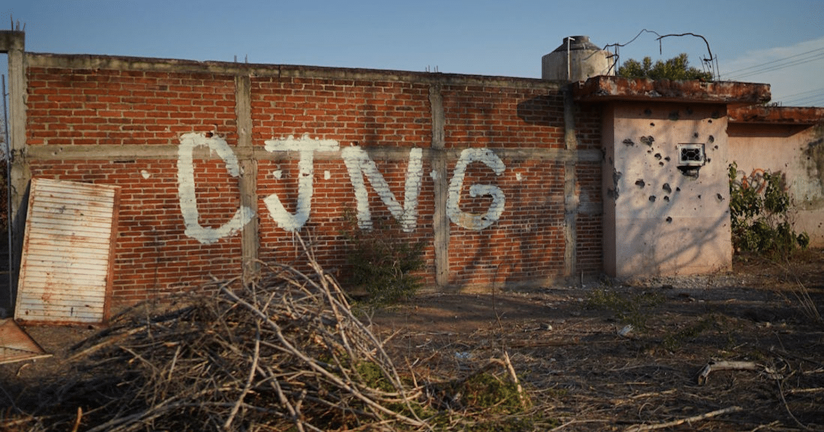 Pared de ladrillo con inscripción 'CJNG', puerta de madera y edificio rosa en Chiapas.